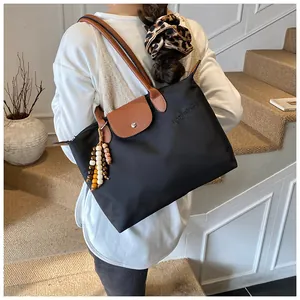Détail du cabas en nylon noir avec rabat en cuir, poignée et breloque en perles