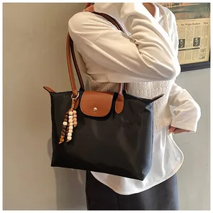 Détail d'un sac cabas en nylon avec anses en cuir marron et breloque perlée