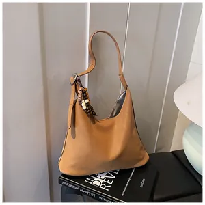 Detailed view of camel suede hobo bag with wooden bead tassel against striped wall