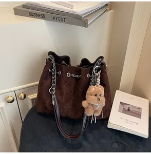 Detail of dark brown quilted suede bucket bag with silver chain strap and plush bear charm