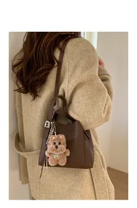 Detail of brown litchi pattern bucket bag with a cute plush bear charm on wool coat
