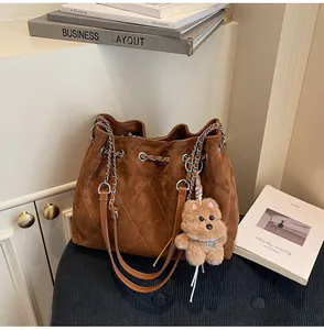 Close-up of brown quilted suede bucket bag with chain strap and teddy bear charm