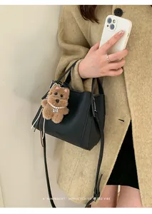 Detail of black lychee leather bucket bag with cute bear charm and fashion text