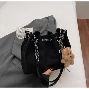 Quilted black bucket bag with silver chain drawstring and plush bear charm on grey blazer