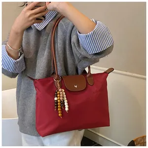 Vue détaillée du cabas en nylon rouge avec anses en cuir et pompon en perles