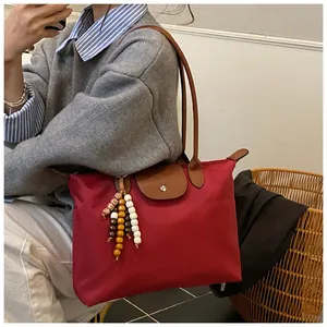 Détail du sac cabas en nylon rouge avec poignée en cuir marron et perles décoratives