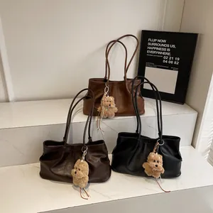 Drie minimalistische suède shopper tassen in bruin en zwart met pluche bedels op een voet