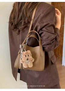 Detail of retro brown leather bucket bag featuring a plush dog pendant with pearl necklace