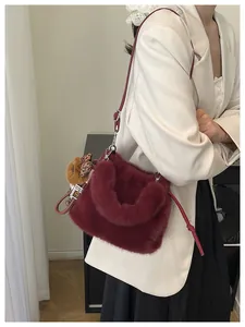 Detail of plush burgundy shoulder bag with furry texture and cute bear charm accessory