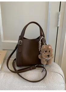 Close-up of brown litchi grain leather bucket bag with plush dog charm and silver hardware