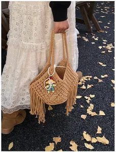 Detail van een bruine handgeweven tas met lange franjes en een schattige poppenhanger