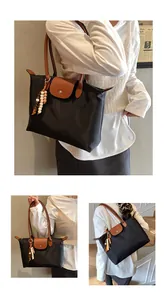 Détail d'un grand sac cabas en nylon avec rabat en cuir, bouton pression et pompon perlé
