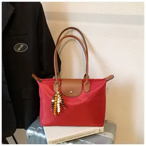 Détail d'un sac cabas en nylon rouge avec poignées en cuir et breloque en perles