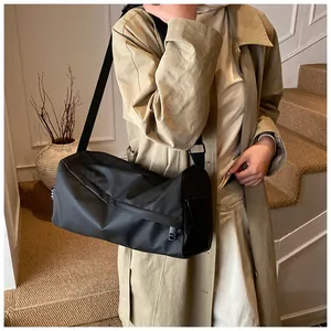 Détail d'un sac noir en tissu Oxford avec poche zippée porté sur un trench-coat beige