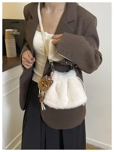 Close-up of a white plush bucket bag with a leopard print bear pendant on a model