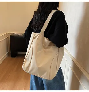 Detail of a beige canvas tote bag showing wide shoulder strap and front pocket embroidery
