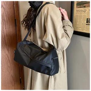 Vue latérale d'un grand sac bandoulière en nylon noir porté avec un trench-coat