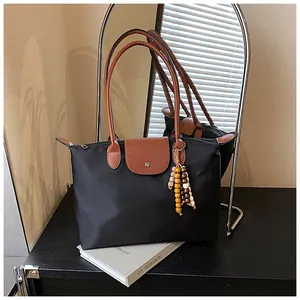 Détail d'un sac cabas en nylon noir avec anses en cuir brun et breloque en perles de bois