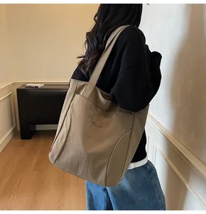 Detail view of khaki canvas tote bag with letter embroidery worn by model in home setting