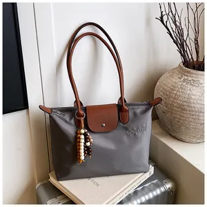 Détail du sac cabas en nylon gris avec poignées en cuir marron et plaque de logo
