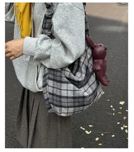 Detail of grey plaid shoulder bag featuring a burgundy leather rabbit charm in autumn setting