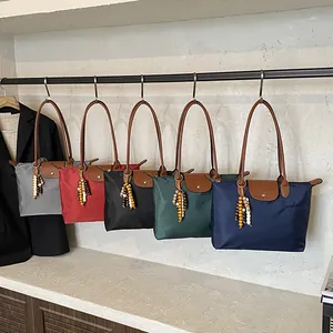 Cinq sacs fourre-tout en nylon avec poignées en cuir et glands suspendus sur un mur épuré