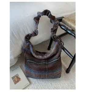 Macro detail of large plaid tote bag featuring textured wool fabric and scrunchie strap