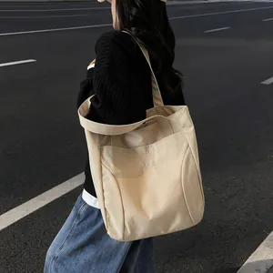 Minimalist cream canvas tote bag with shoulder straps worn by model in street scene
