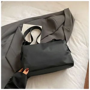 Détail d'un sac bandoulière en tissu Oxford noir posé sur un lit avec accessoires