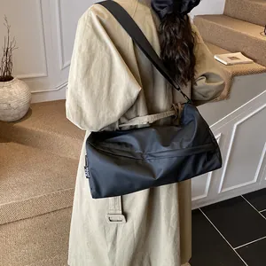 Grand sac bandoulière en nylon noir porté par un mannequin en décor minimaliste
