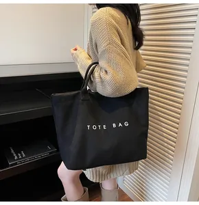 Detail of a large black canvas tote bag with TOTE BAG print worn by a woman