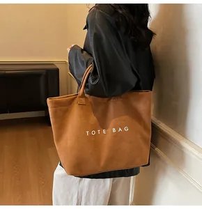 Detail of a large brown suede tote bag with white TOTE BAG lettering shown on a model