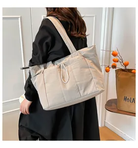 Detail view of a large beige quilted tote bag with drawstring, worn by a female model