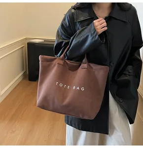 Detail of a brown suede tote bag with white TOTE BAG lettering and sturdy handles