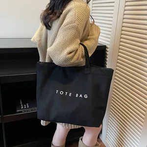 Black canvas tote bag with white TOTE BAG lettering shown on a model in a minimal room