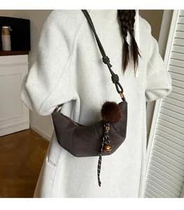 Vue détaillée du sac croissant en daim marron foncé avec pompon et bandoulière nouée