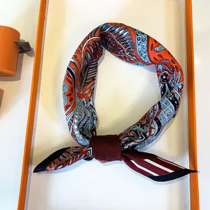 Detail of silk twilly scarf with orange floral pattern tied in a soft loop knot