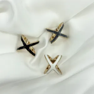 Close-up of three X-shaped enamel scarf rings in black, grey, and white on silk fabric