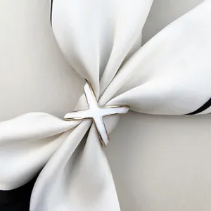 Detailed close-up of X-shaped silk scarf buckle in gold finish with white enamel inlay