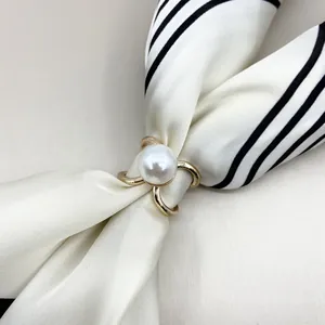 Close-up of gold V-shaped scarf clip with white pearl on black and white silk scarf