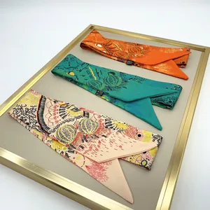 Trois foulards en soie avec motifs botaniques dans un plateau de présentation doré