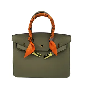 Détail d'un foulard en soie orange noué sur la poignée d'un sac à main en cuir vert grainé