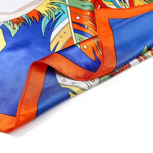 Gros plan d'un foulard en satin aux motifs de plumes tropicales avec bordure orange