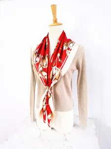 Detail of red and white floral silk scarf with golden ring buckle on a beige cardigan