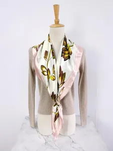 Close-up of a large square silk scarf with floral branch pattern and golden scarf ring buckle
