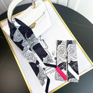 Elegant camellia print skinny silk scarf in black and white tied on a luxury bag handle