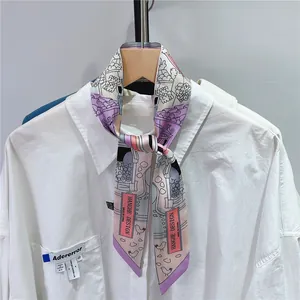 Detail eines Seidenschals mit Vogel- und Hausmuster an einer weißen Hemdbluse