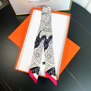 Macro detail of camellia print twilly silk scarf presented in a luxury orange gift box