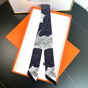 Close-up of black and white camellia silk scarf twilly in luxury orange gift box