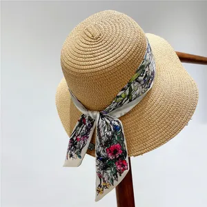 Detail of a natural woven straw sun hat featuring a colorful floral ribbon bow on a wooden hook